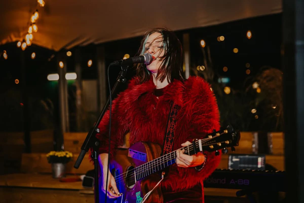Vibrant live music performance with female singer playing guitar on stage under string lights.