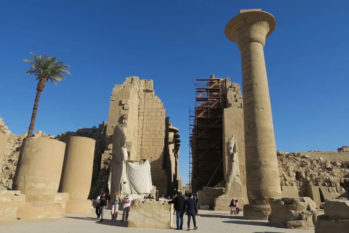 Visitors explore the historical Karnak Temple ruins in Luxor, Egypt on a sunny day.
