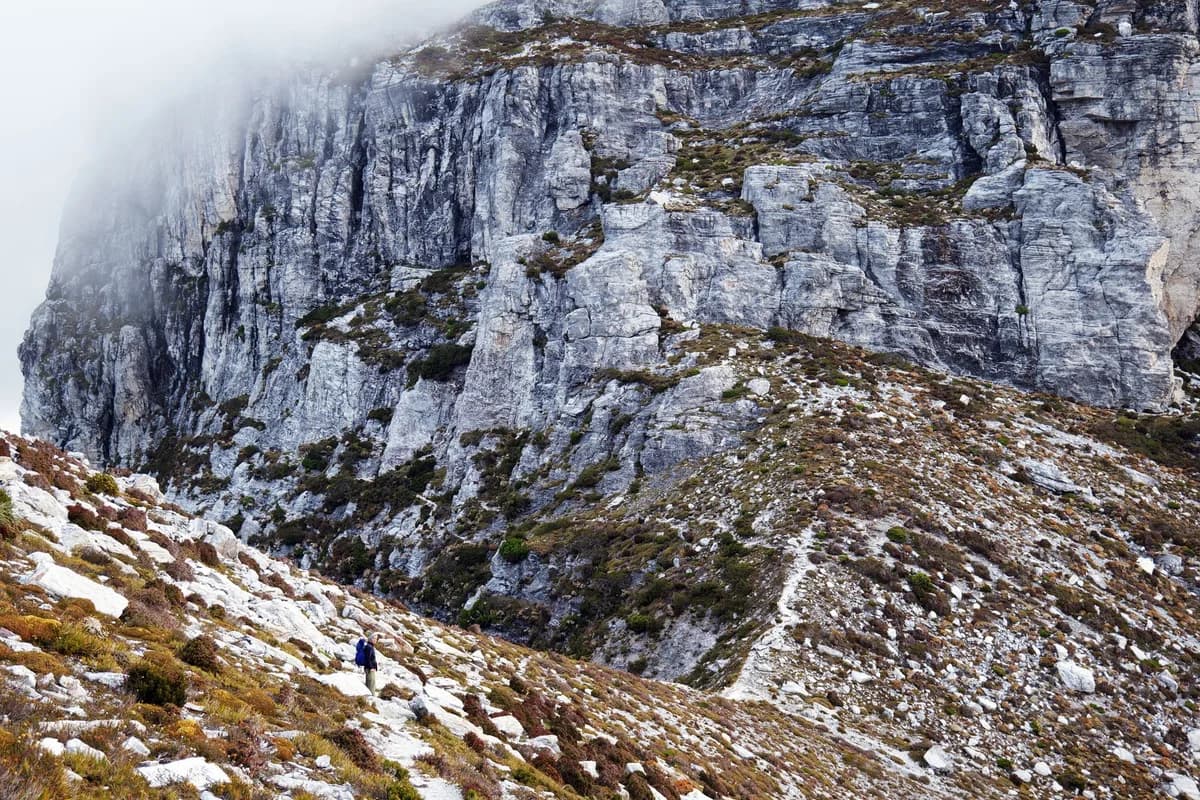 A lone hiker traversing the rocky slopes of Tasmania's rugged landscape, perfect for adventure enthusiasts.