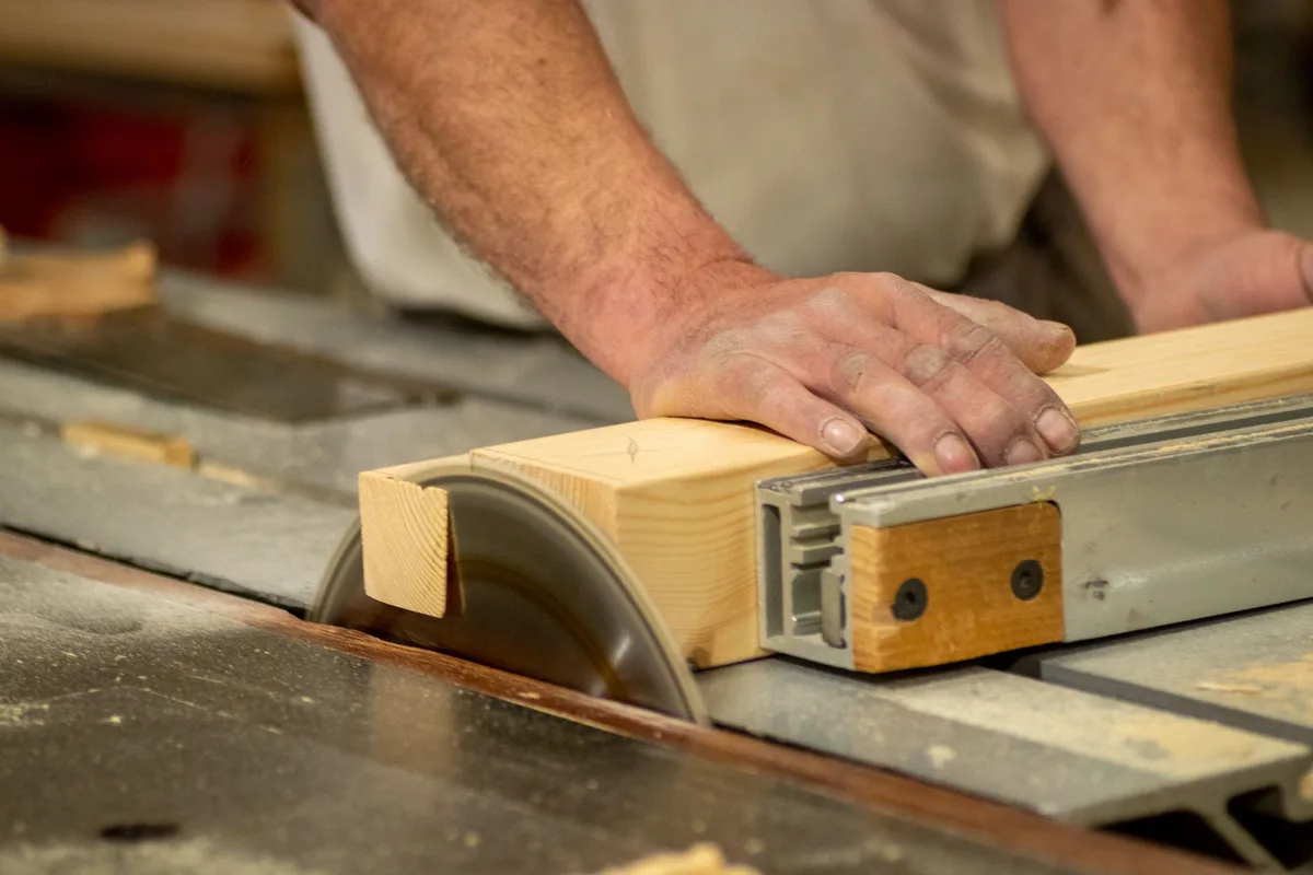 Hands of a carpenter cutting wood on a table saw, showcasing craftsmanship and precision.