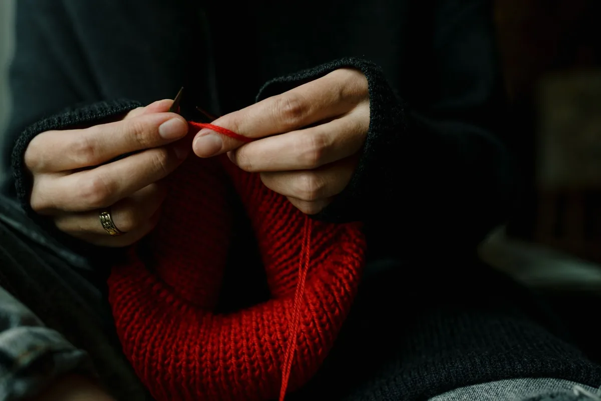 Detailed view of hands carefully knitting red wool yarn, showcasing intricate craftsmanship.
