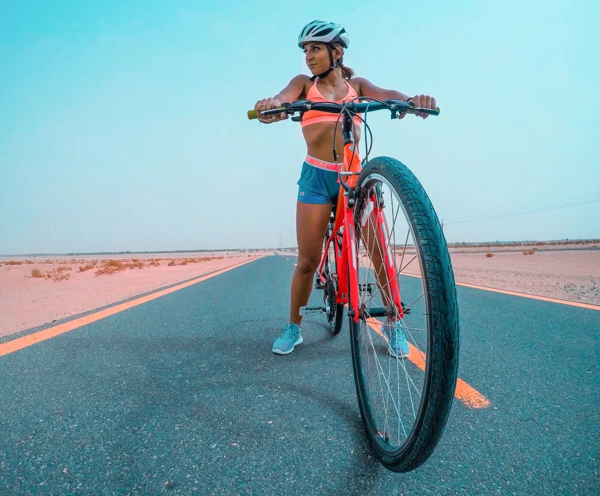 A woman cyclist in athletic gear on a bike in the Dubai desert, promoting fitness and adventure.