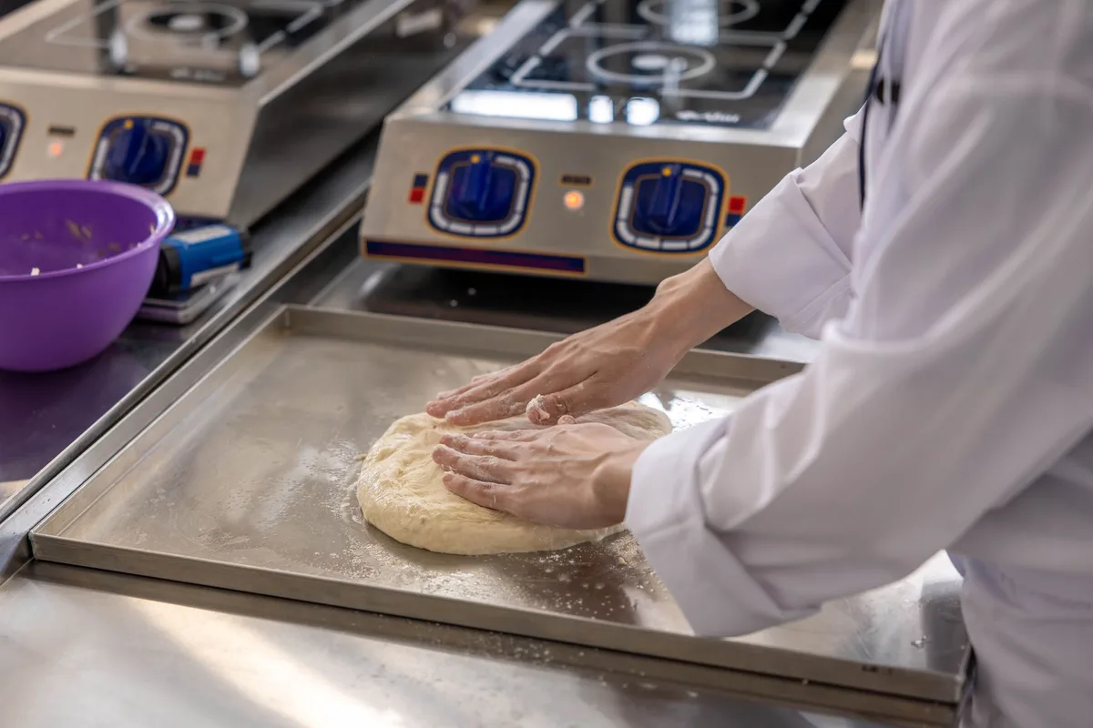 A chef is kneading dough on a stainless steel counter in a commercial kitchen.