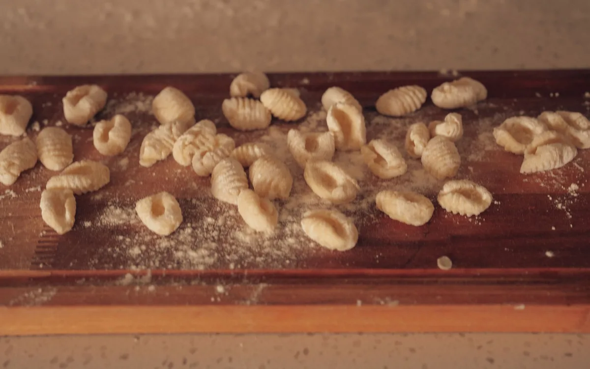 Raw gnocchi scattered on a wooden board lightly dusted with flour.