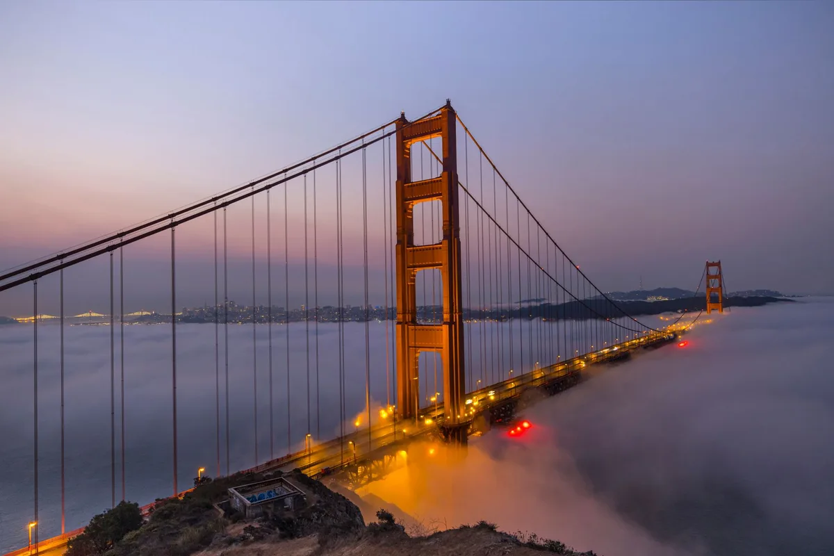 Golden Gate Bridge enveloped in morning fog under a colorful dawn sky.