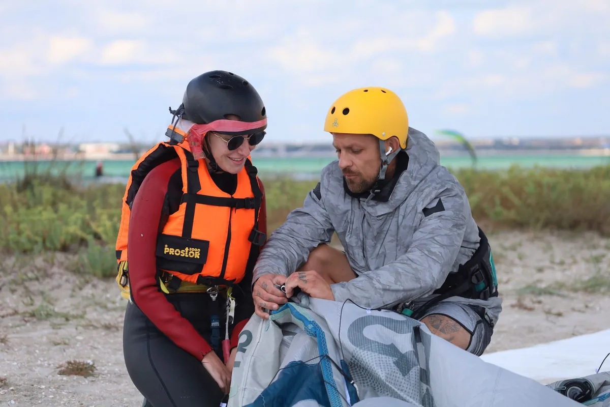 Instructors teaching kitesurfing with safety gear on a sunny beach.