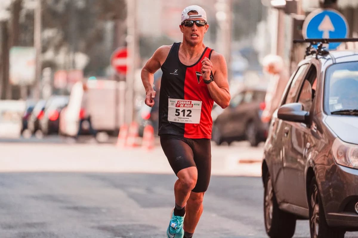 Athletic man wearing a cap and sunglasses competing in a marathon on urban streets.
