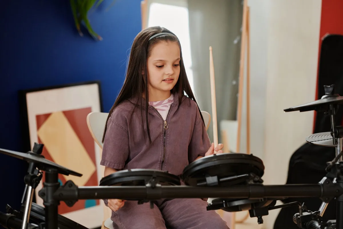 Girl with long hair skillfully playing electronic drums indoors, showcasing talent.