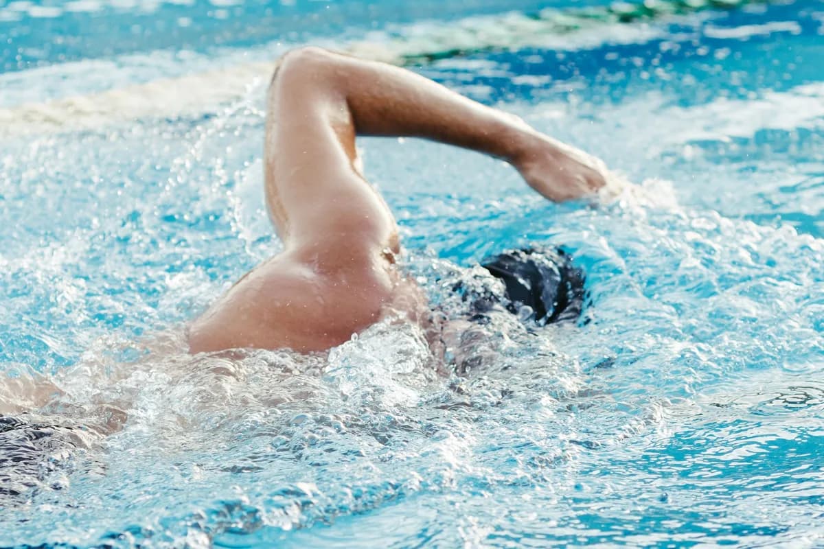 Adult male swimmer practicing freestyle stroke in outdoor pool during daytime training session.