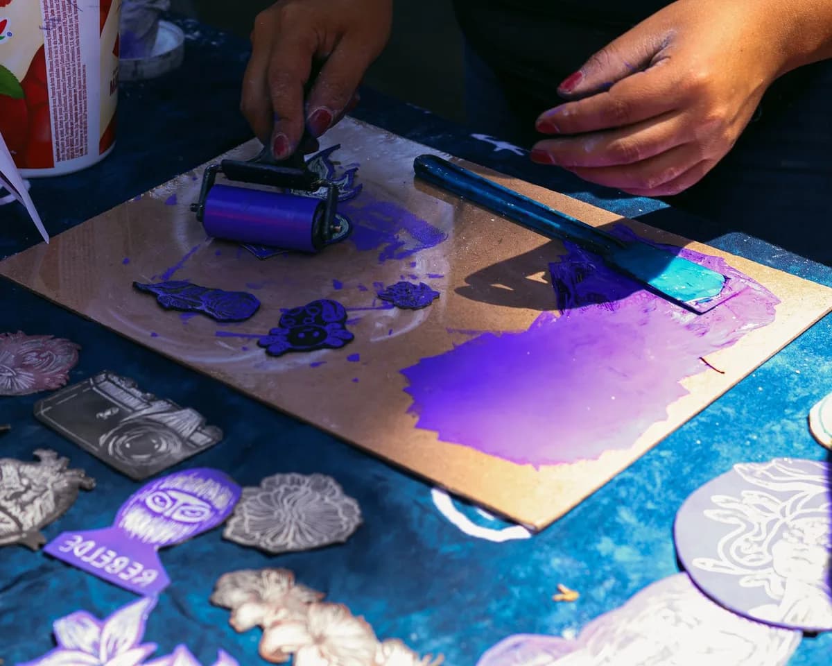 Artist working with purple ink on linocut prints. Hands engaged in creative process with vibrant colors.
