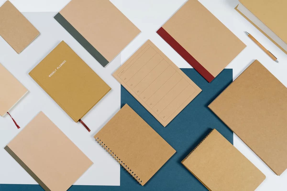 Elegant flat lay of various brown spiral notebooks and planners on a blue background.