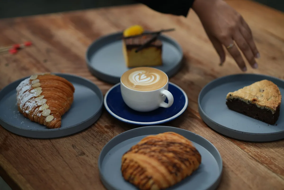 Assorted pastries and latte art coffee on a wooden table, hand in action.