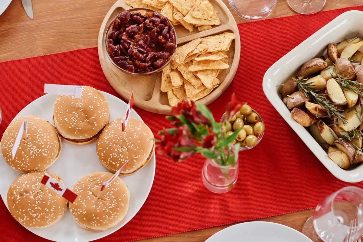 Top view of a festive Canadian-themed table with burgers, nachos, and roasted potatoes.