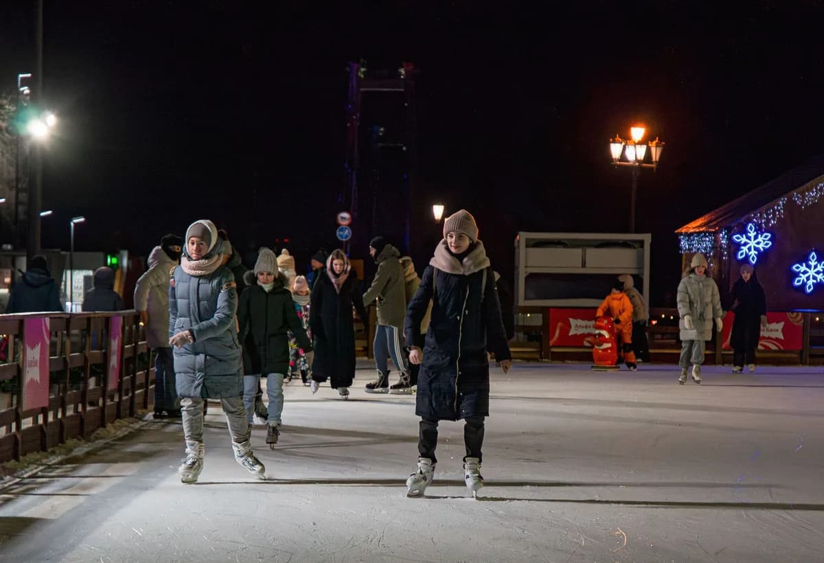 People enjoy ice skating on a well-lit outdoor rink at night.