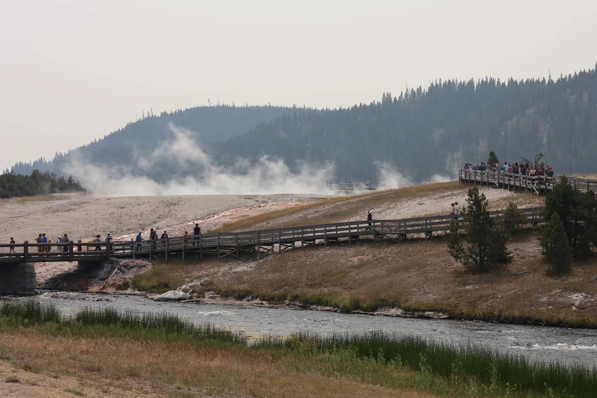 Visitors walk along boardwalk near steaming geysers in Yellowstone.