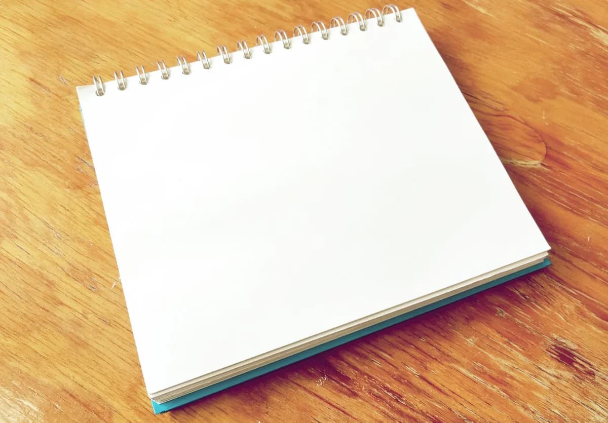 A blank spiral notebook lies open on a wooden desk, perfect for notes or sketches.