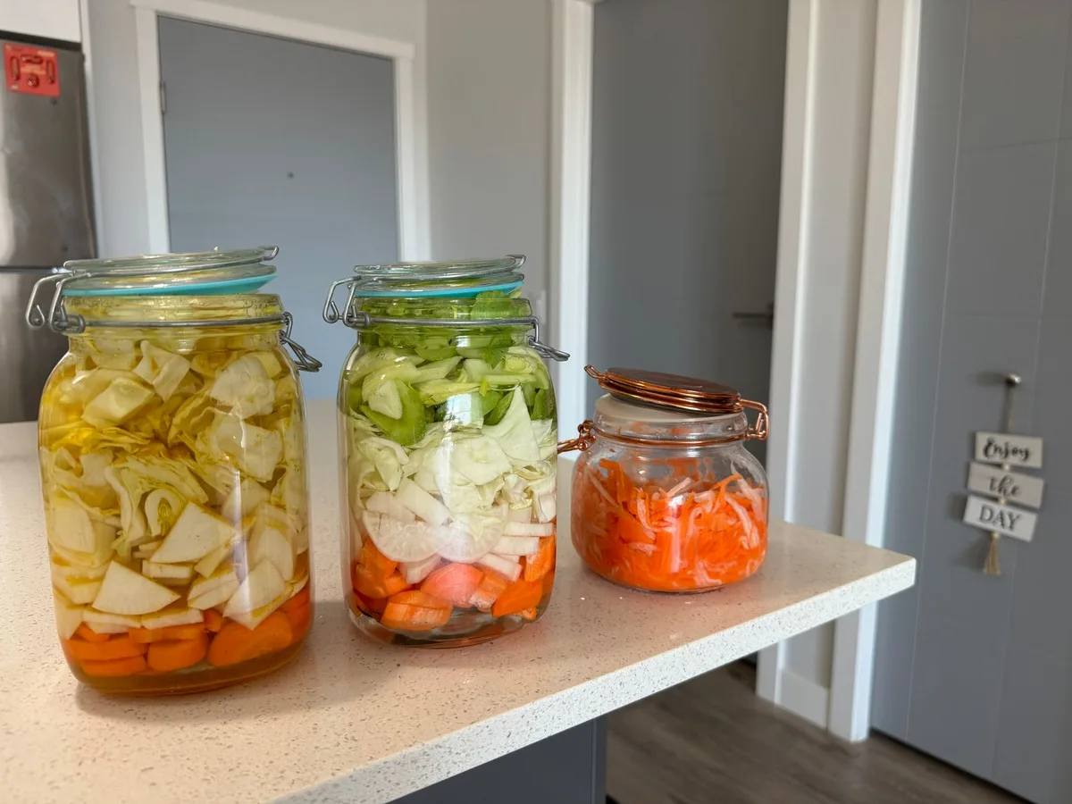 Three jars filled with colorful homemade pickled vegetables on a kitchen counter.
