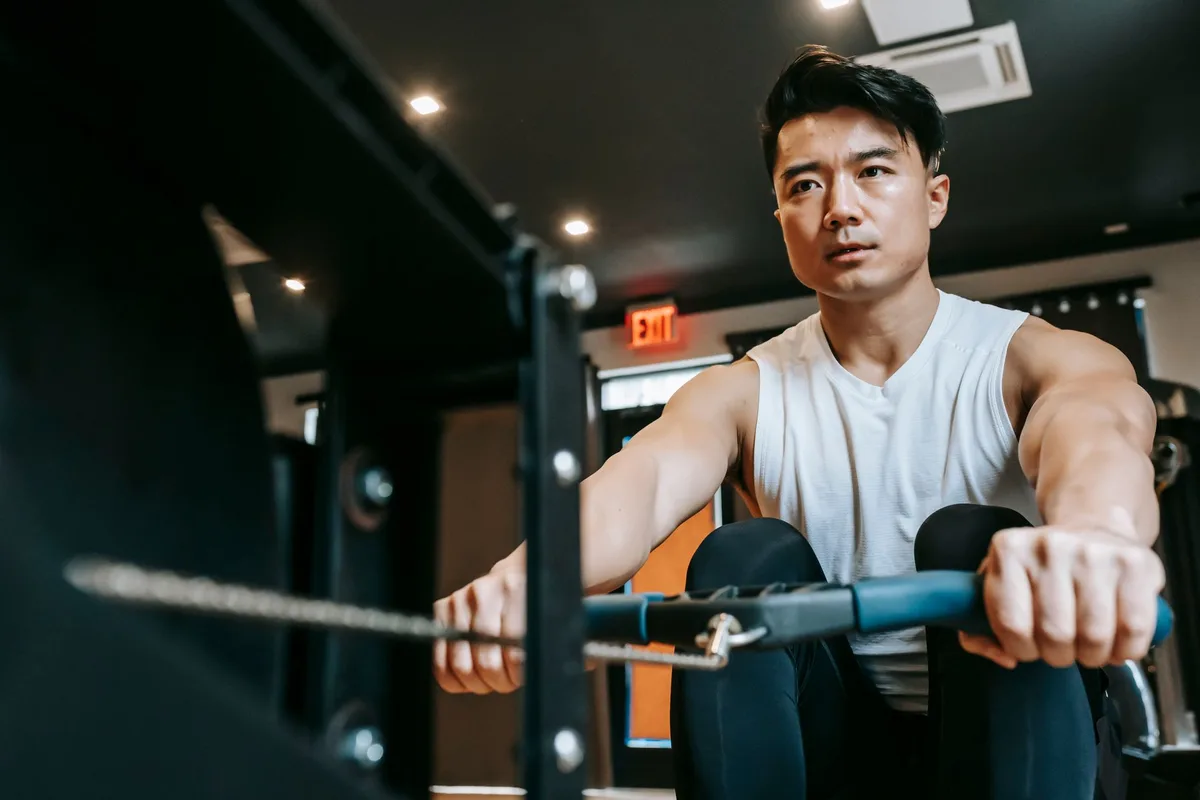 Low angle of determined muscular male sportsman intensively training and looking forward while exercising on machine