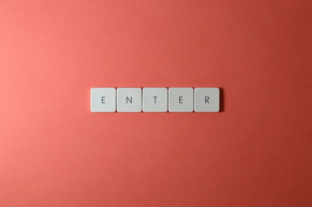 Close-up of five keyboard letter tiles spelling 'ENTER', placed on a coral backdrop.