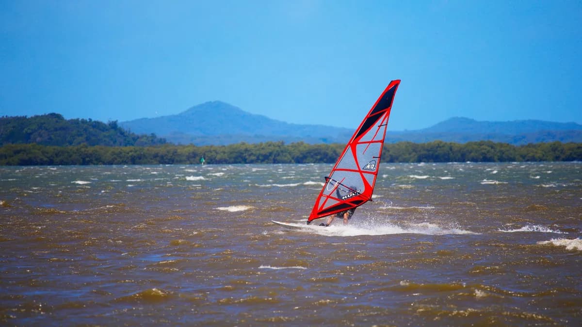 A windsurfer navigates the waves with a vivid sail against a scenic mountain backdrop.