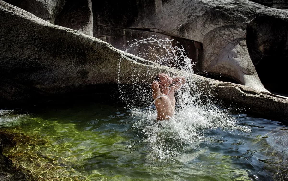 An adult man joyfully splashing water in a natural rock pool, creating a splash. Perfect summer outdoor activity image.