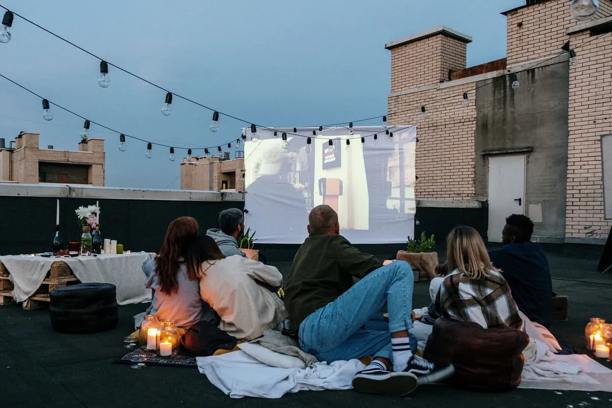Friends enjoying a cozy rooftop movie night with candles and blankets under string lights.