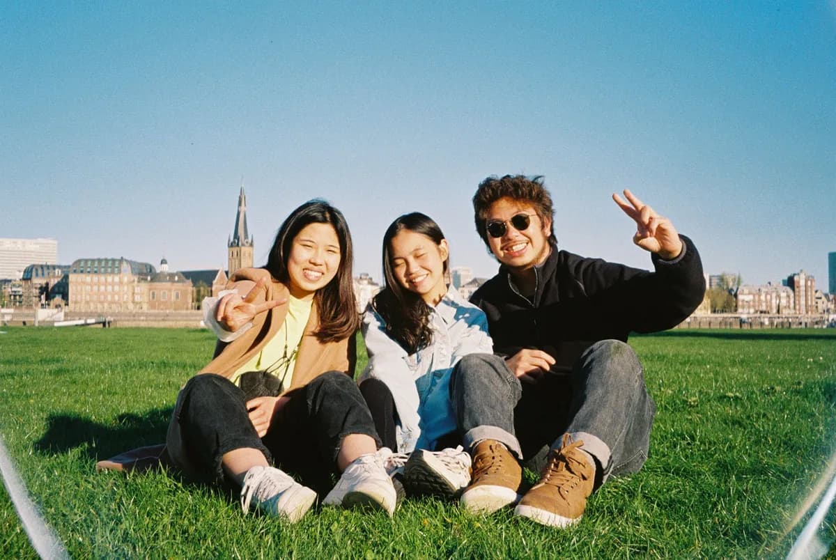 Three friends smiling and enjoying a sunny day in a Düsseldorf park, capturing youthful joy.