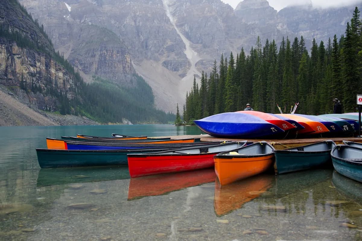 Vivid canoes lined up on a serene lake with mountain backdrop and lush forest.