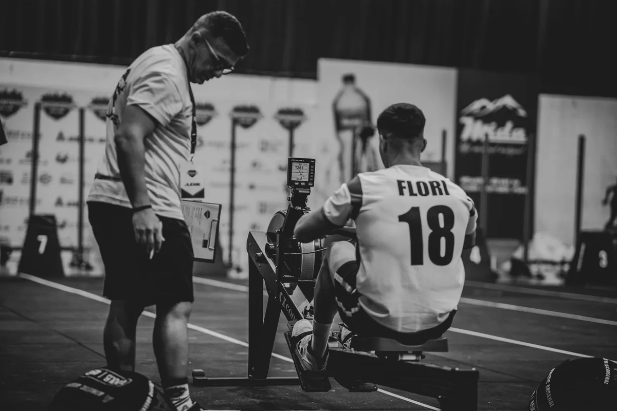 An athlete using a rowing machine indoors, coached in a gym setting.