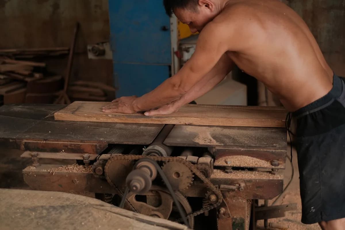 A shirtless man skillfully operates a table saw in a woodworking workshop.