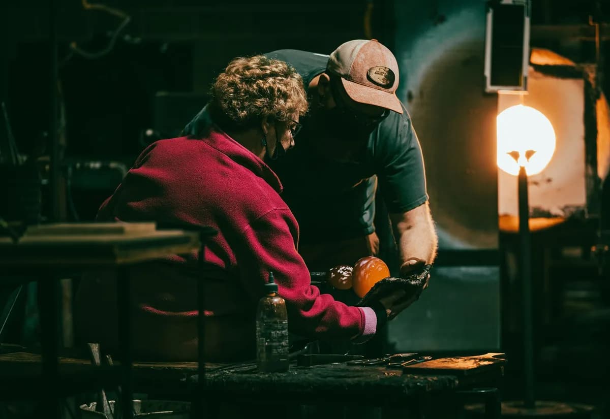 Two people shaping molten glass in a glassblowing workshop.