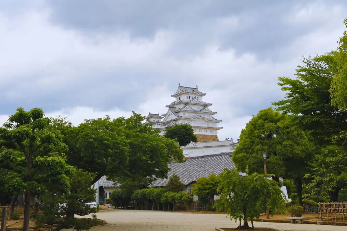 A captivating view of Himeji Castle in Hyogo, Japan, framed by lush trees under a cloudy sky.