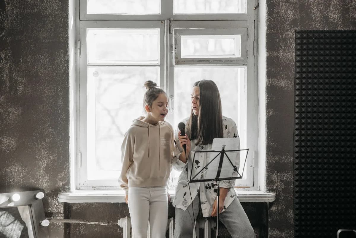 A young girl and her teacher practicing singing in a music studio.