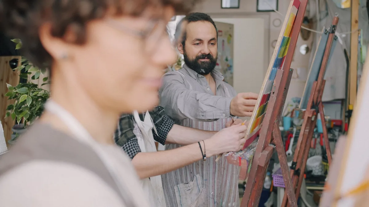 Group of artists painting together in a bright, indoor studio setting.