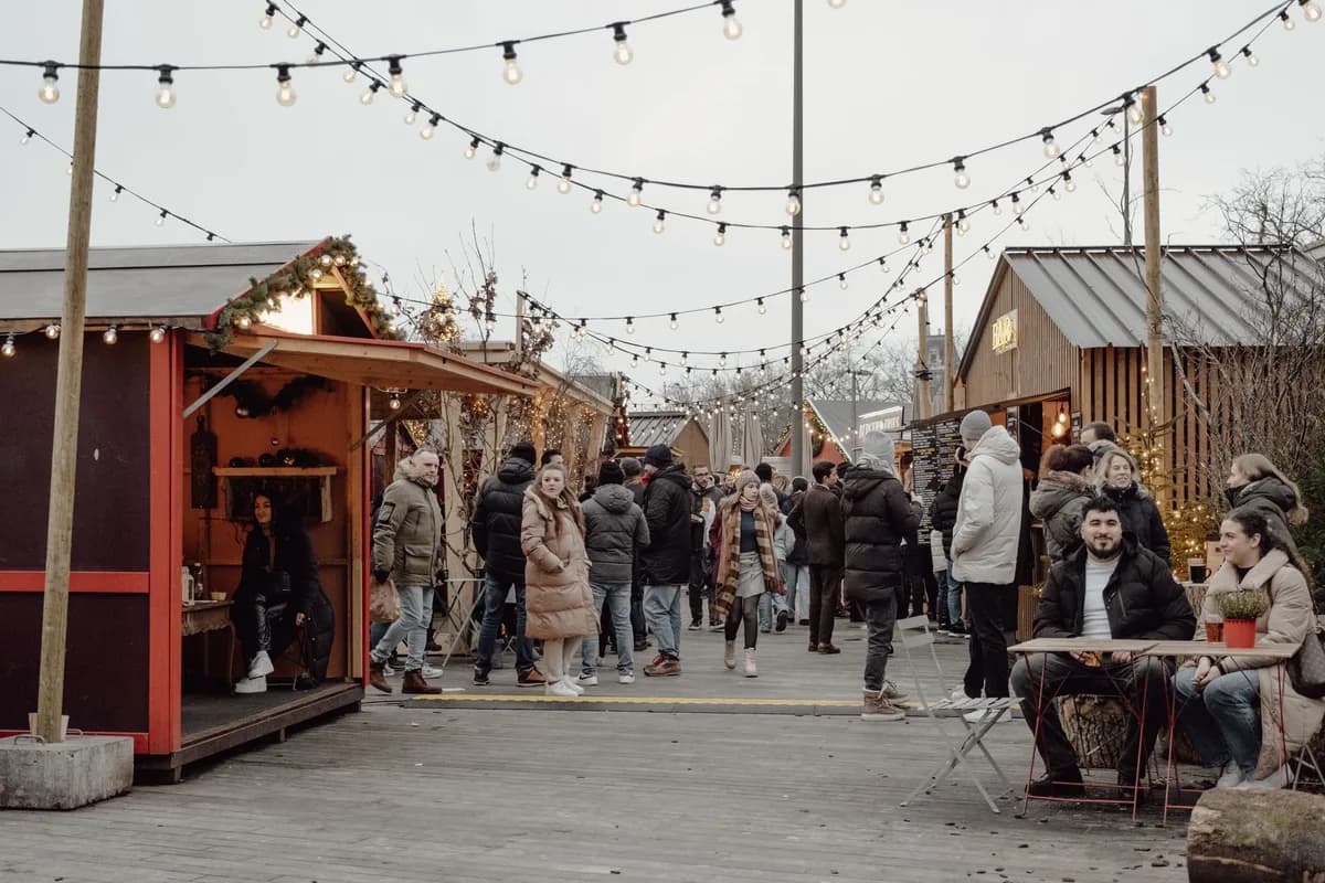 Festive winter market in Zurich with people enjoying food and shopping under string lights.
