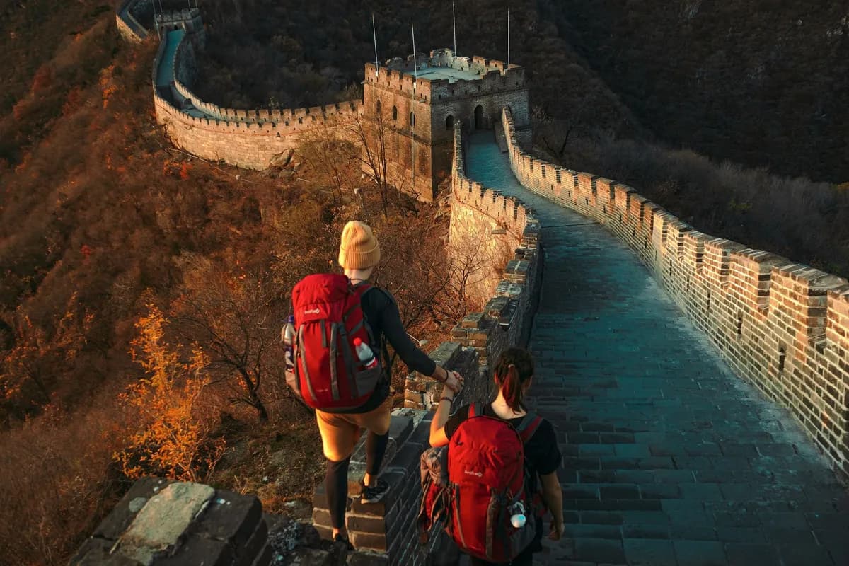 Two hikers on Great Wall, exploring ancient architecture during a sunny autumn day.