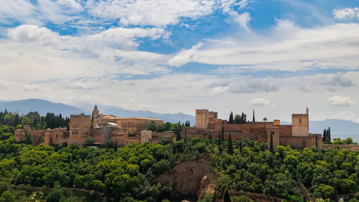 A scenic view of the Alhambra Palace surrounded by greenery under a vibrant blue sky in Granada, Spain.