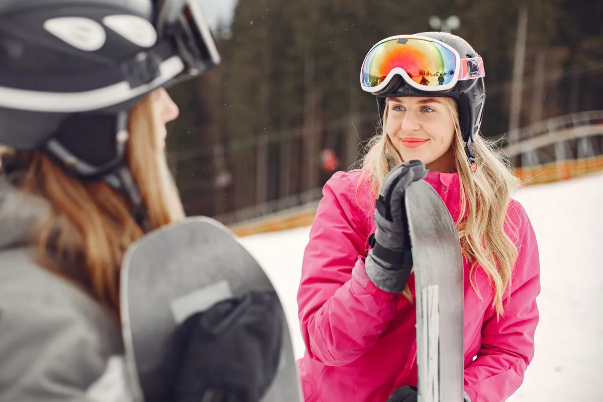 Two women enjoying snowboarding in a winter landscape, wearing helmets and gear.