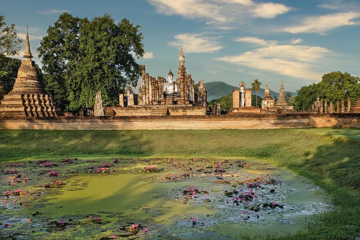 Serene view of ancient temples and blooming lotus pond in Sukhothai, Thailand.