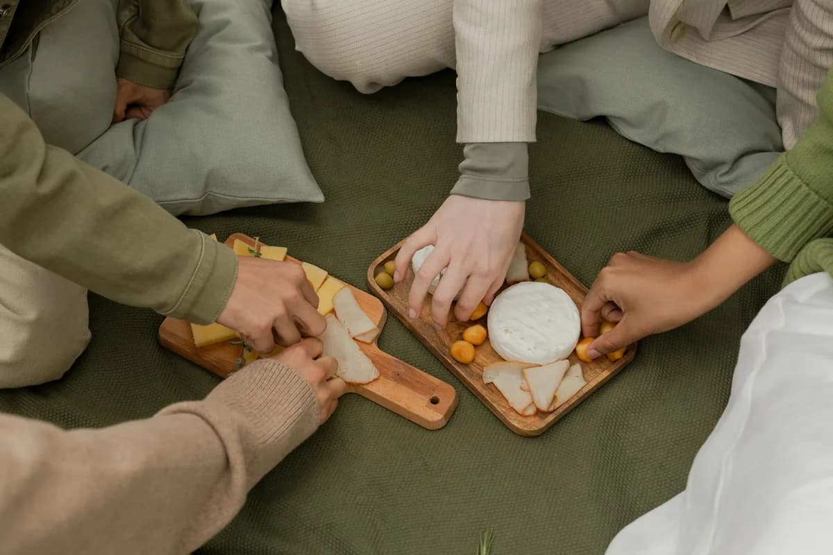 A group of friends sharing and enjoying a delicious cheese platter during an outdoor picnic.