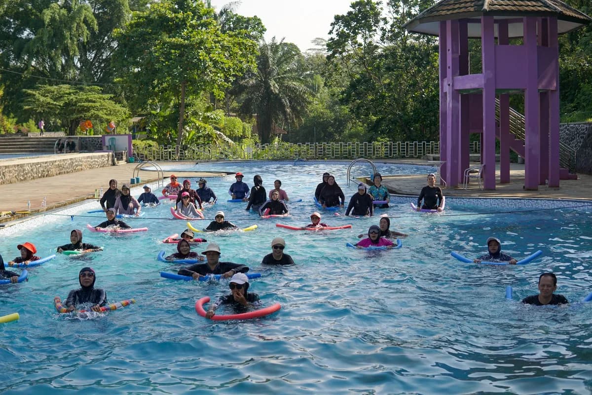 A large group of people enjoying water exercises with float devices in an outdoor pool in West Java, Indonesia.