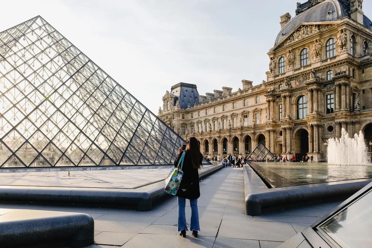 A tourist admires the iconic Louvre Pyramid and historic museum architecture, Paris.
