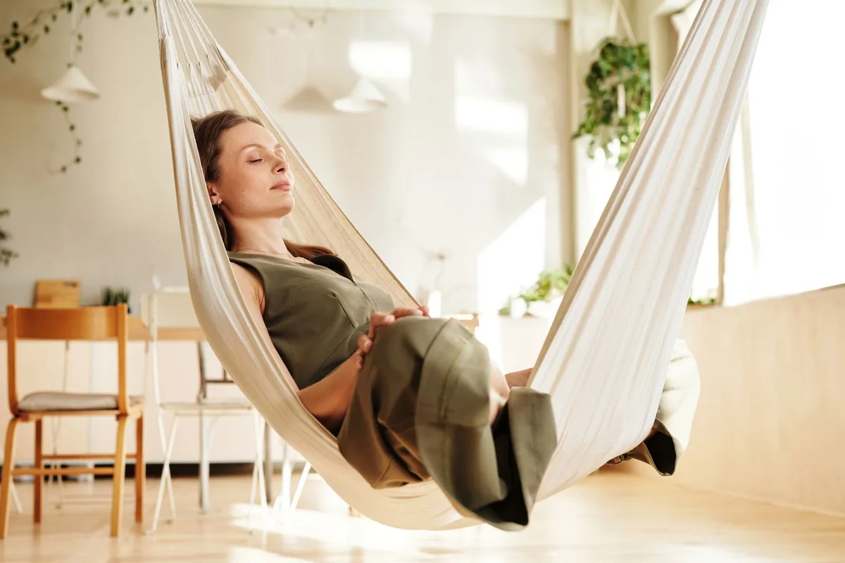 A woman enjoys a peaceful nap on an indoor hammock under soft natural light.