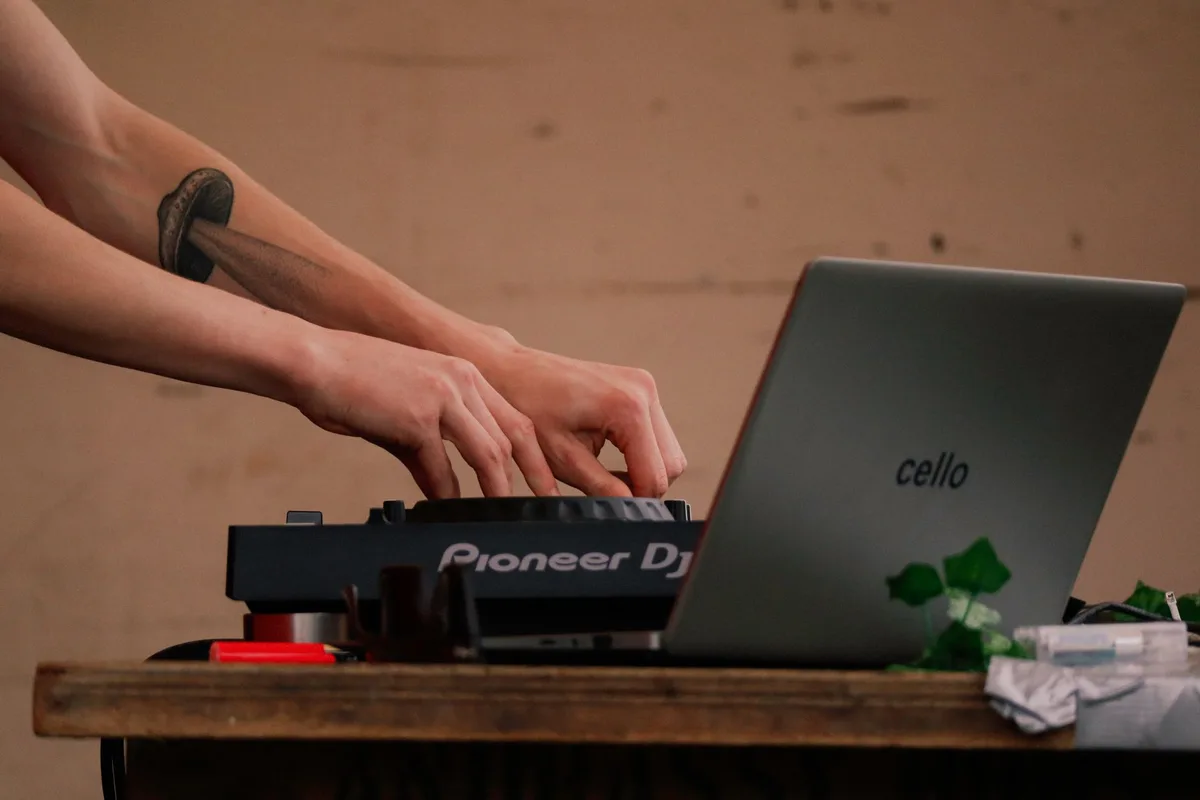 Close-up of hands mixing music using a Pioneer DJ controller next to a laptop.