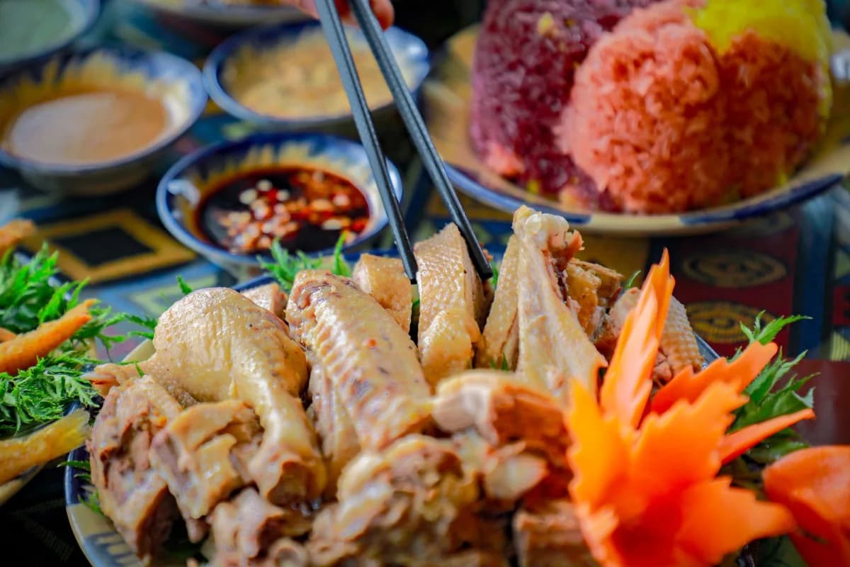 Close-up of a traditional Asian chicken dish with chopsticks, colorful rice, and vegetables.