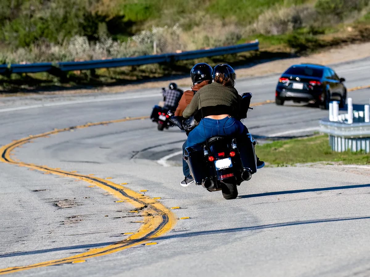 Group of motorcyclists navigating a curvy road in a scenic rural setting, showcasing adventure and freedom.