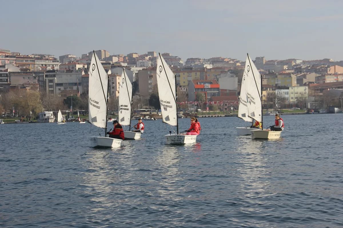 Children sail in small boats on İstanbul's city waters, surrounded by an urban backdrop.