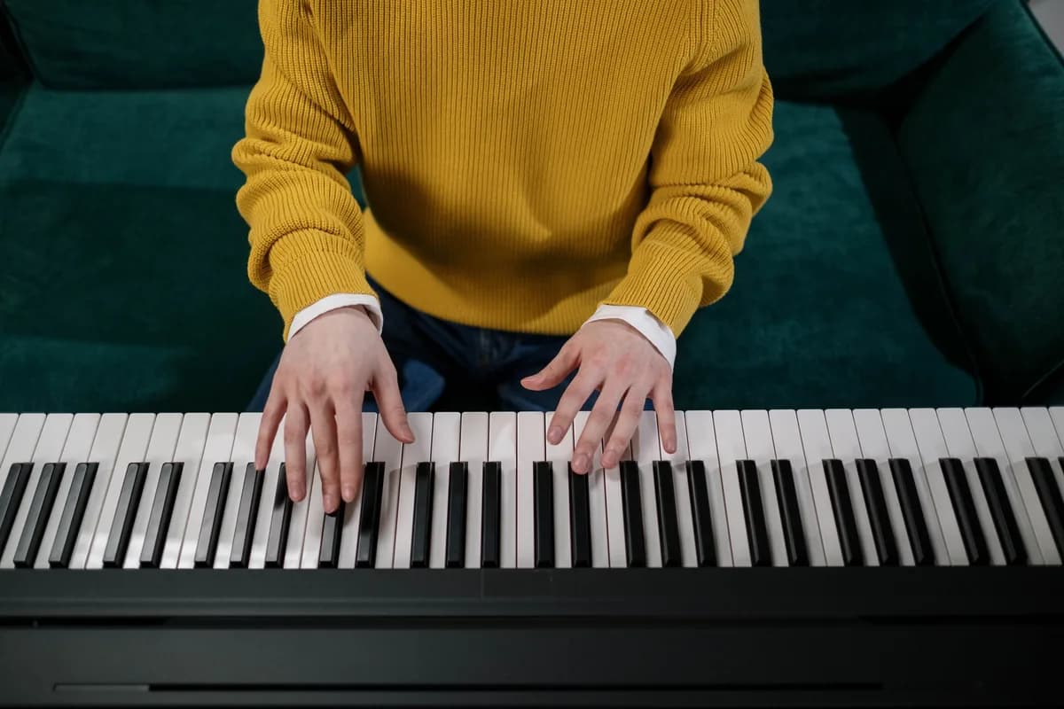 Top view of a person playing piano in a yellow sweater, focusing on the hands and keys.