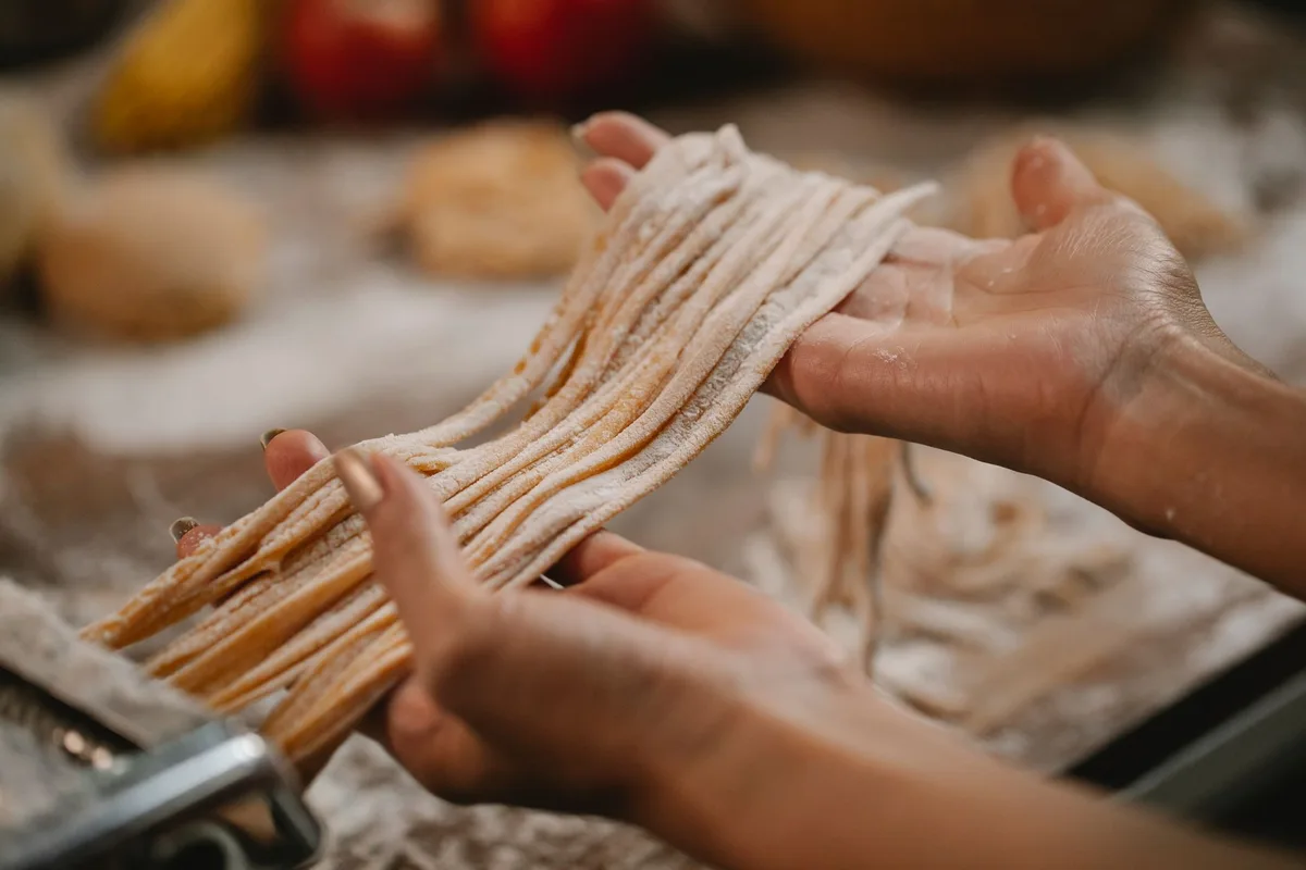 Crop anonymous female producing spaghetti with pasta cutter on blurred background of table