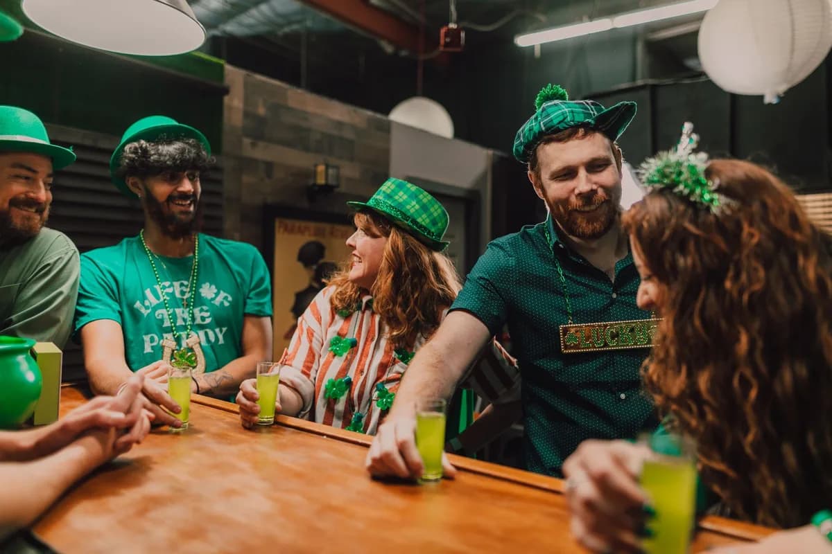 Group of friends enjoying St. Patrick's Day party with themed outfits and drinks.